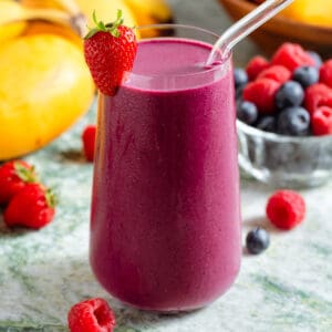 A tall glass with bright purple maqui berry smoothie and a glass straw garnished with a strawberry.