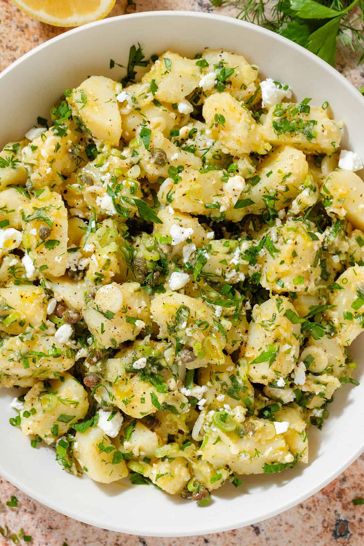 Potato salad with lemon vinaigrette, lots of chopped fresh herbs in a beige serving bowl.