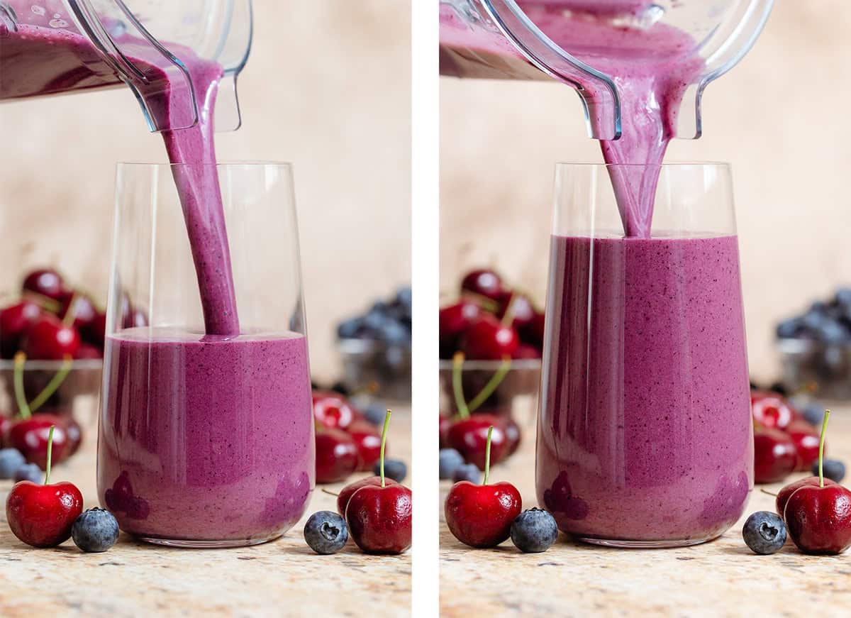 Vibrant purple smoothie being poured into a tall glass with cherries and blueberries around it.