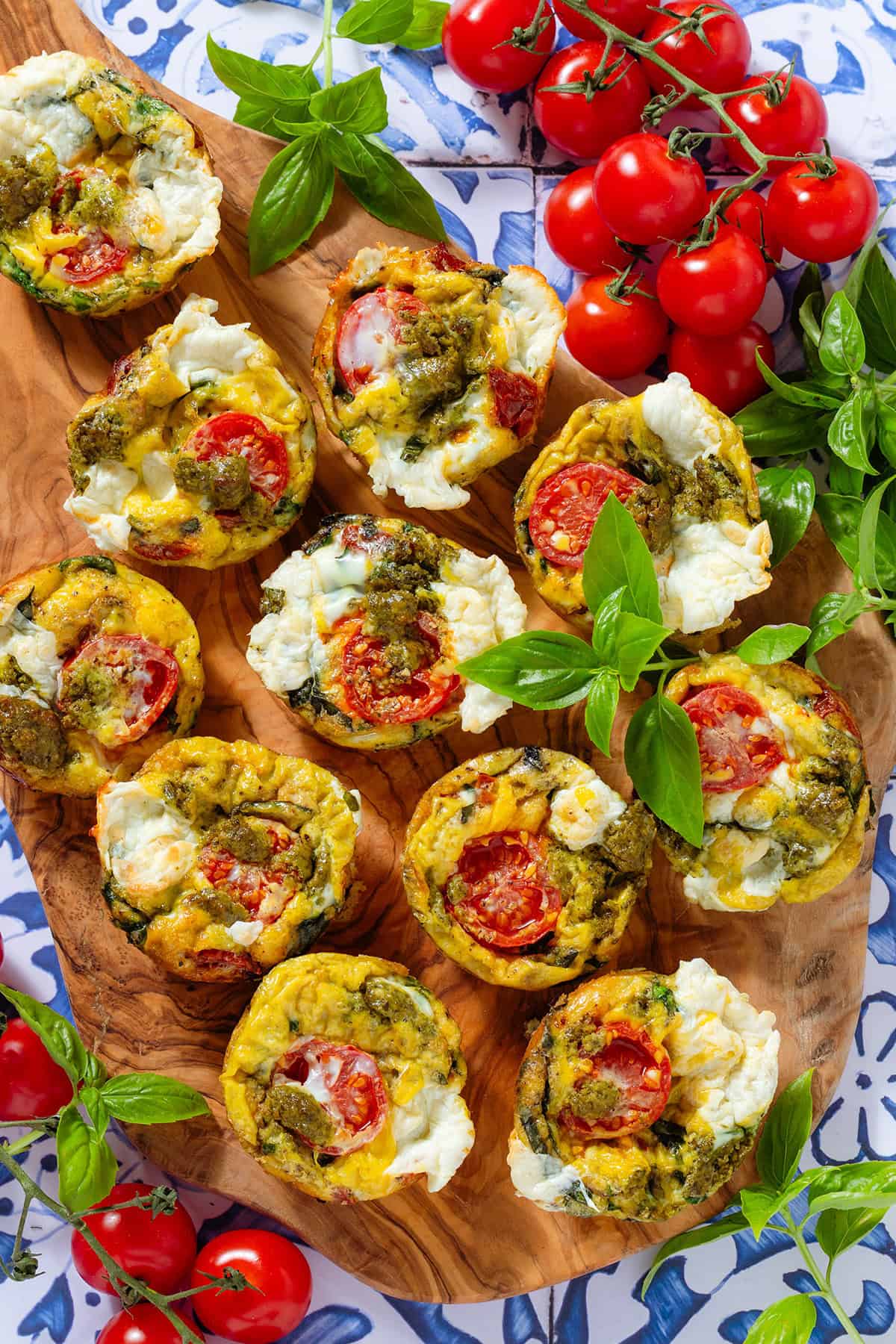 Caprese egg muffins on a wooden serving board garnished with fresh basil and cherry tomatoes around it.
