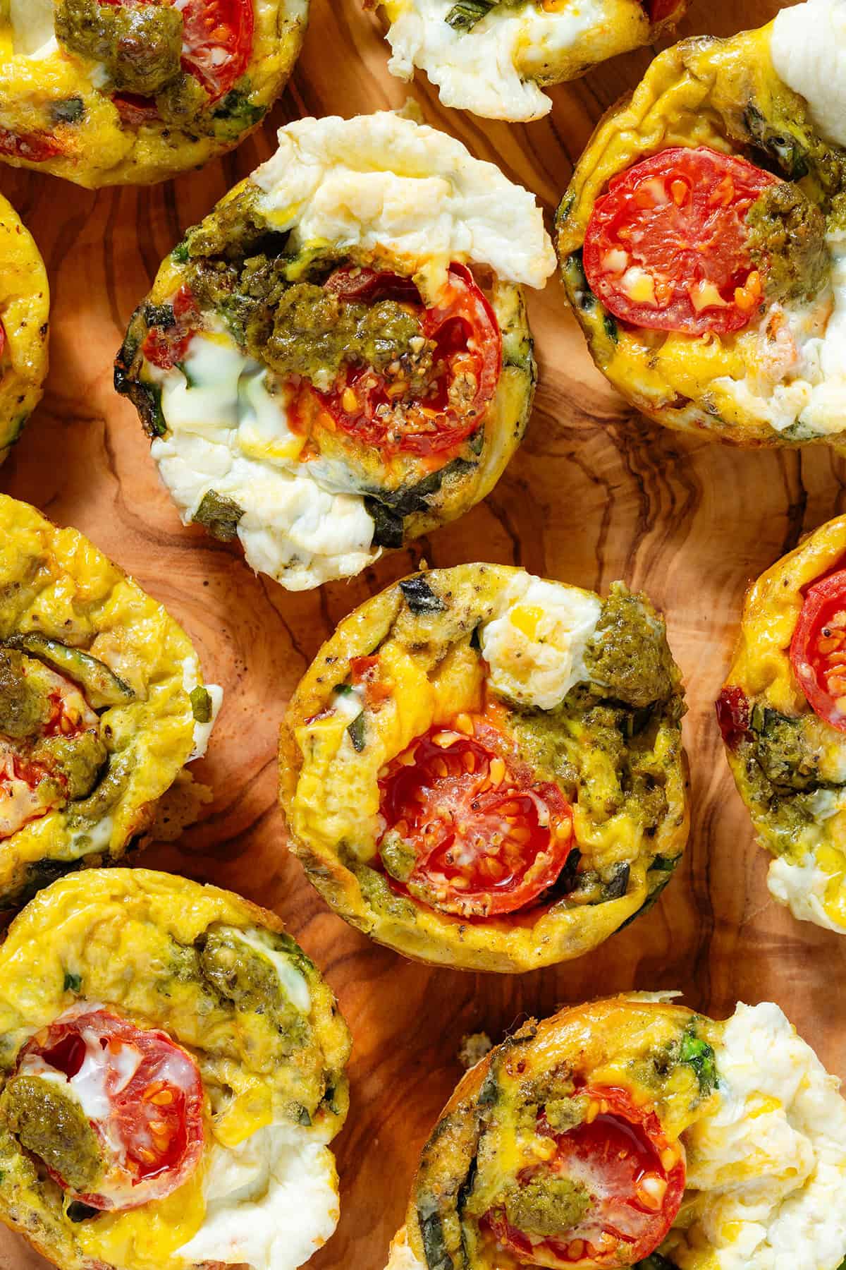Egg bites with mozzarella, pesto, cherry tomatoes and other ingredients served on a wooden serving board.
