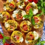 Caprese egg muffins on a wooden serving board garnished with fresh basil.