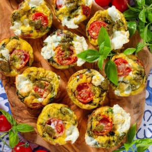 Caprese egg muffins on a wooden serving board garnished with fresh basil.