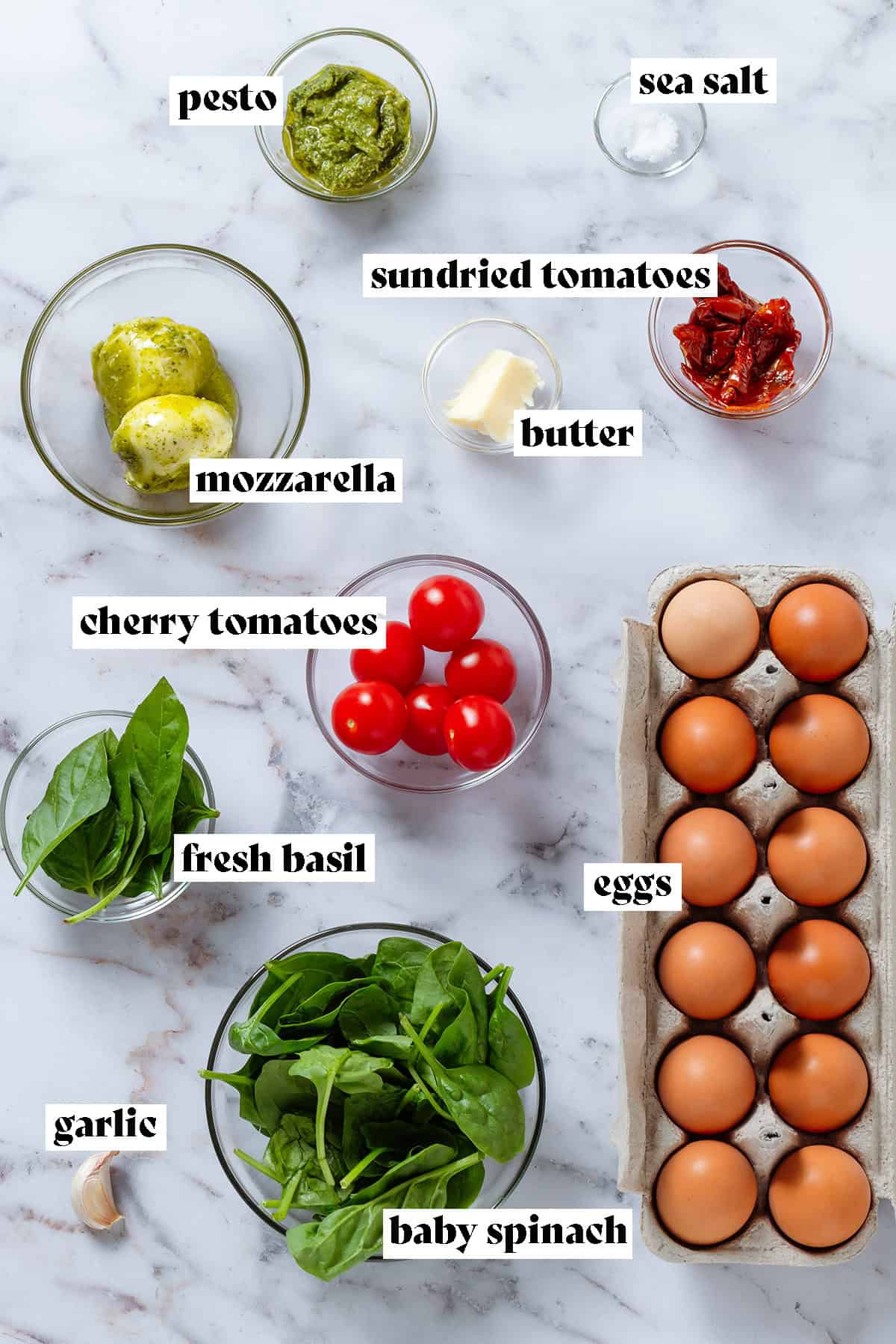 Ingredients in glass bowls like spinach, cherry tomatoes, mozzarella, sundried tomatoes, and basil, and eggs in a carton on the right with text overlay.