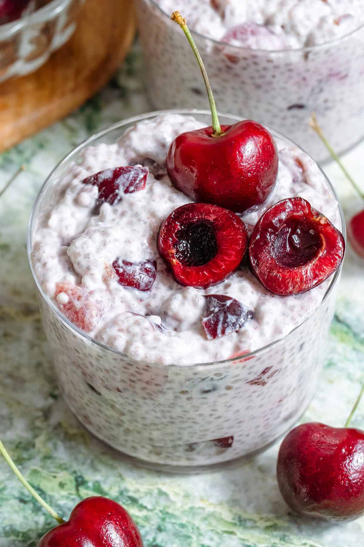 Cherry chia pudding in a short glass garnished with one whole cherry and one cherry sliced in half and pitted and with more cherries around the glass.