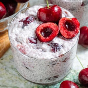 Cherry chia pudding in a small glass garnished with one whole cherry and one cherry sliced in half and pitted.