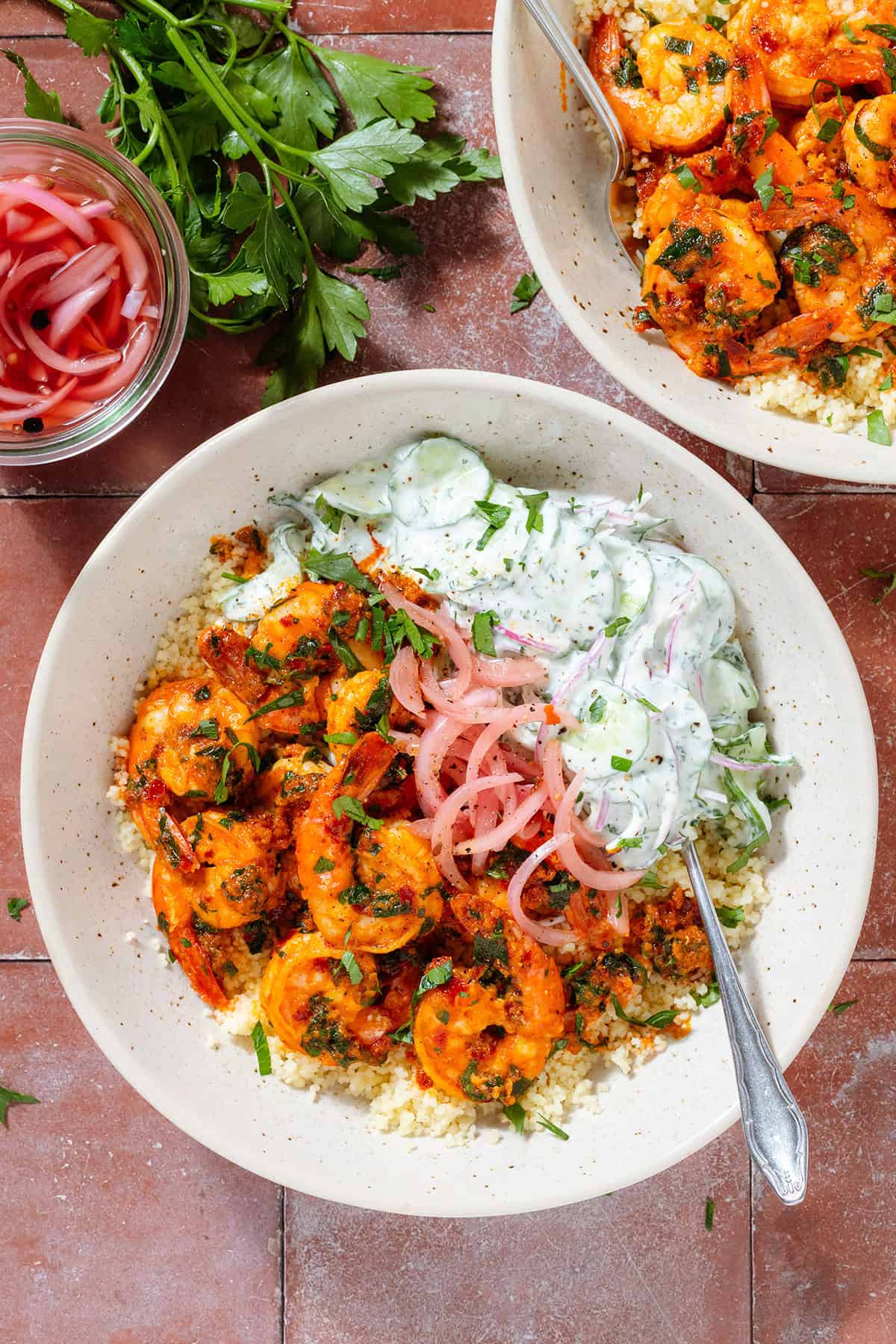 Low bowls with harissa shrimp atop Moroccan couscous, with creamy cucumber salad and pickled red onion.