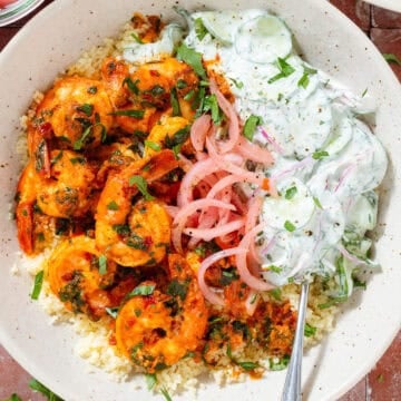A bowl with harissa shrimp served on Moroccan couscous, with creamy cucumber salad and pickled red onion.