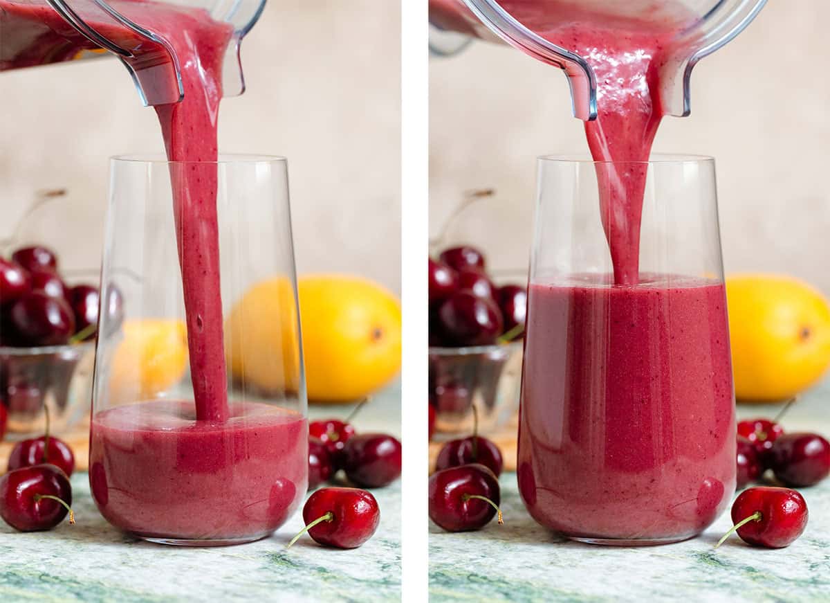 A cherry mango smoothie being poured into a tall glass with the same fresh fruit around it.