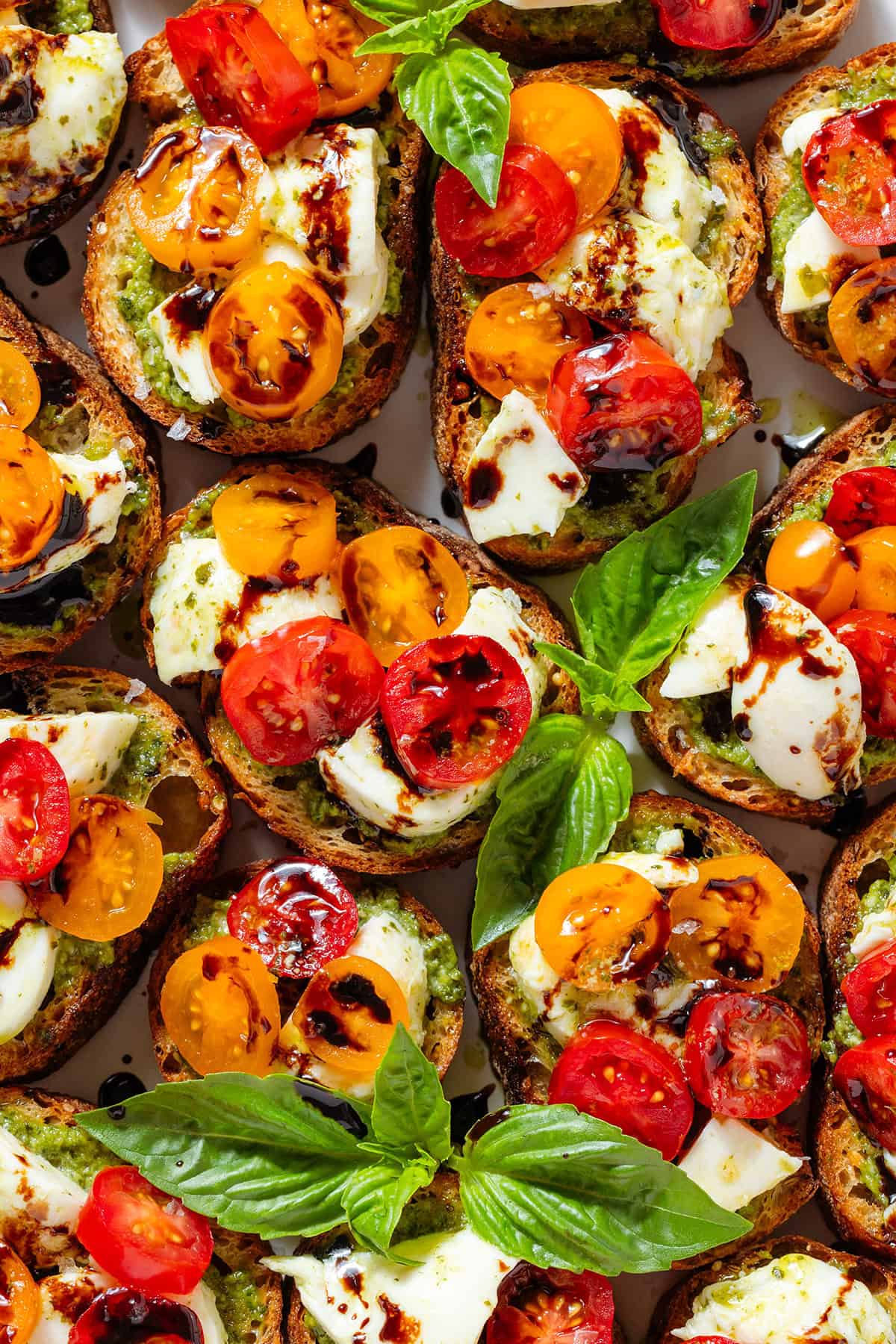 Crostini with pesto, mozzarella, cherry tomatoes drizzled with balsamic glaze and garnished with fresh basil leaves and flaky sea salt.