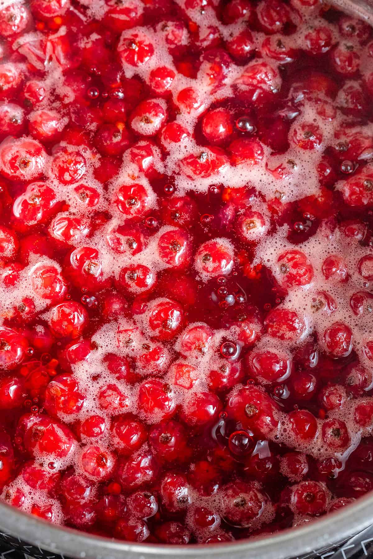 Red currants gently simmering with water and sugar in a small saucepan on the stove.