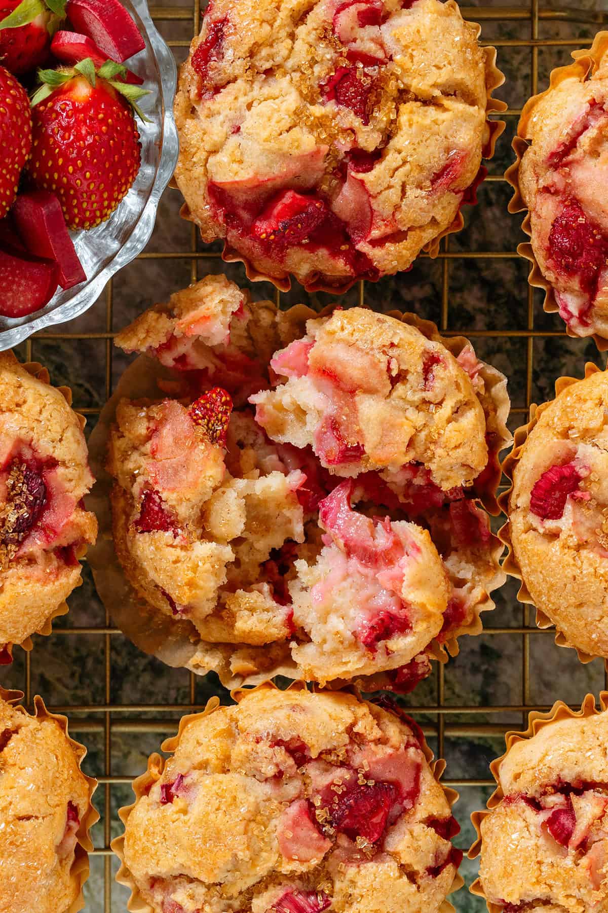 Strawberry rhubarb muffins on a gold wire rack with the middle on pulled apart to show the soft and fluffy inside.