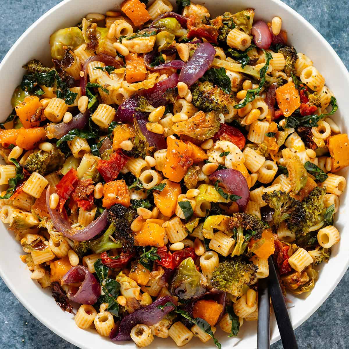 Fall pasta salad with mixed fall and winter vegetables, fresh mozzarella, pine nuts, and sundried tomato dressing in a large shallow bowl.