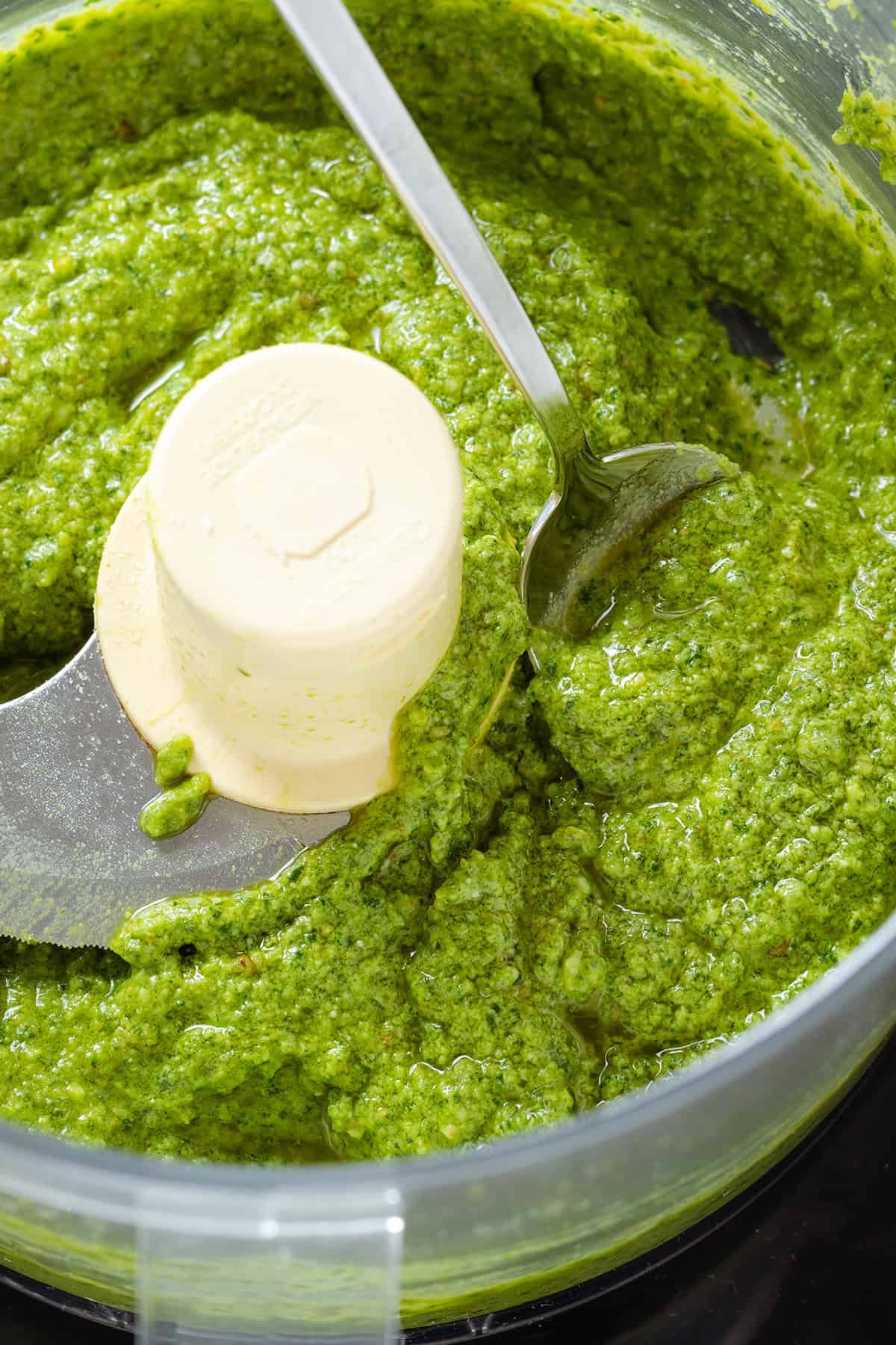 Blended pesto in a food processor with a spoo scooping it up.