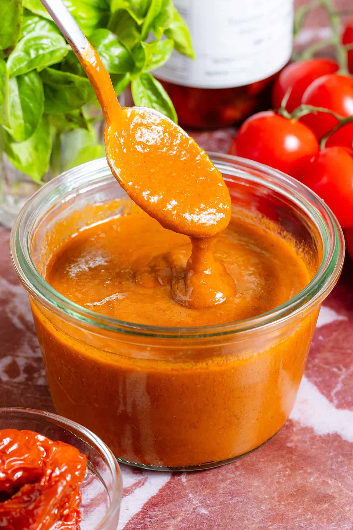 A glass jar of homemade blended sundried tomato vinaigrette and a spoon scooping it up to show how creamy it is.