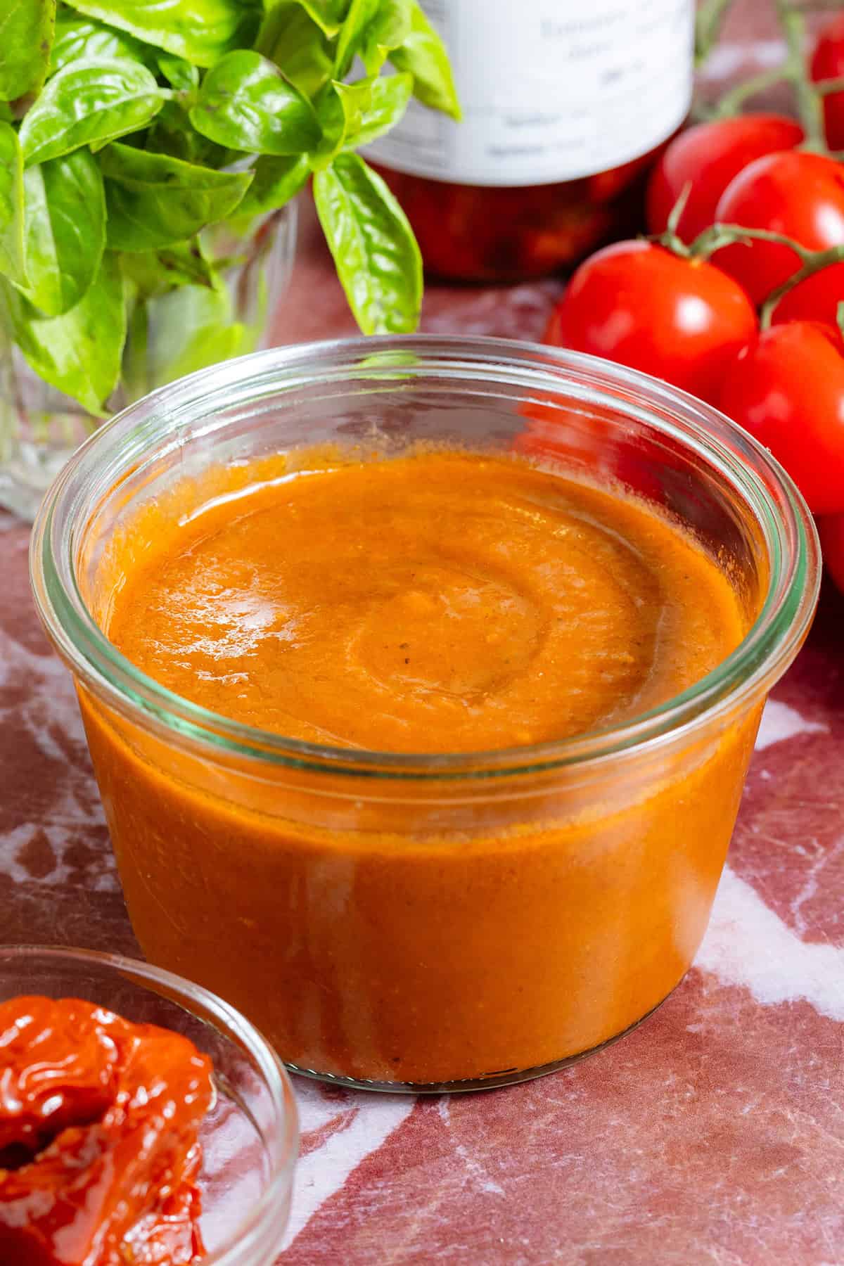 Blended sundried tomato vinaigrette in a glass jar surrounded with tomatoes and fresh basil.