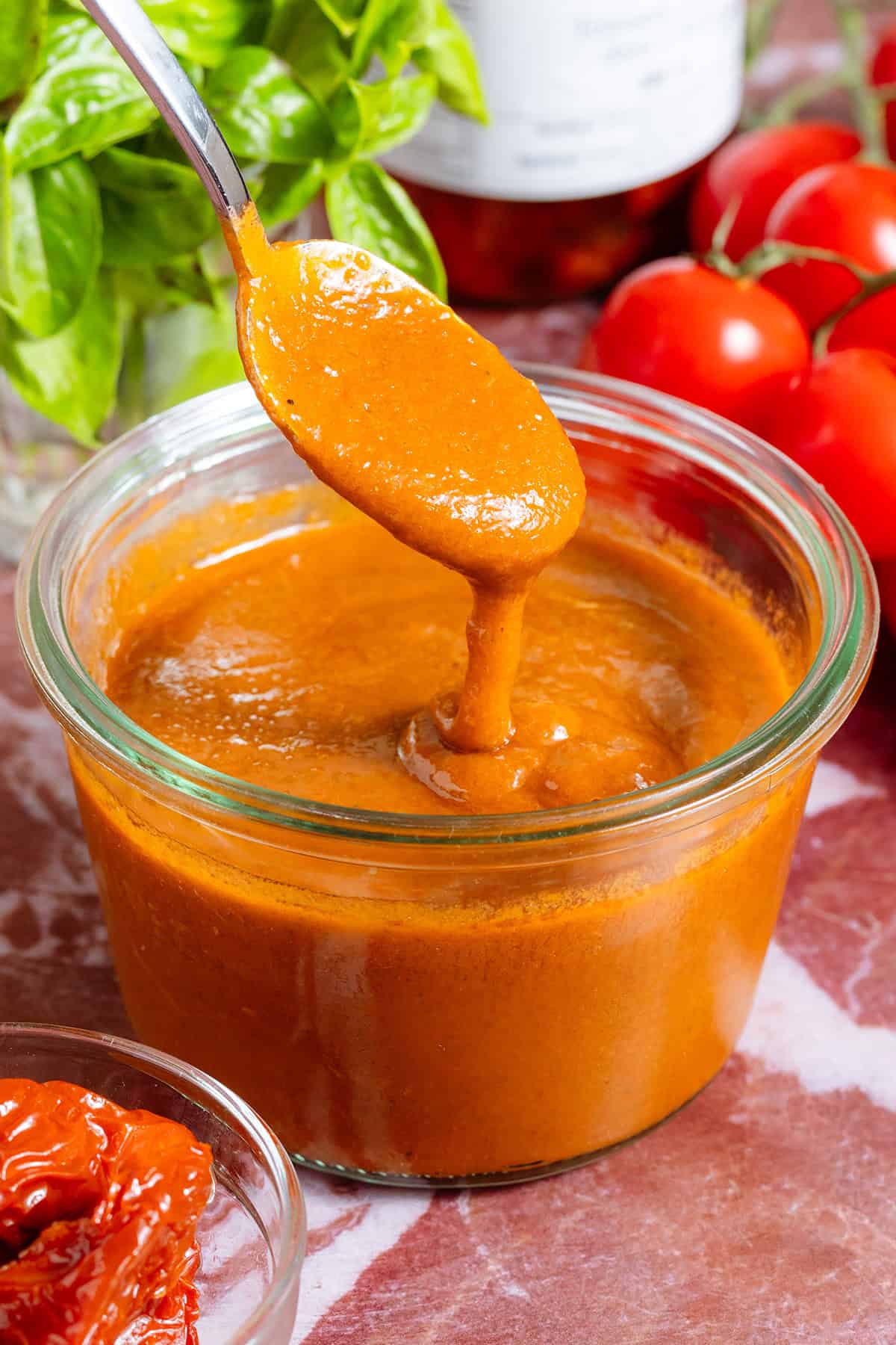 A glass jar of homemade blended sundried tomato vinaigrette and a spoon scooping it up to show how creamy it is.