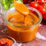 A glass jar of homemade blended sundried tomato vinaigrette and a spoon scooping it up to show how creamy it is.